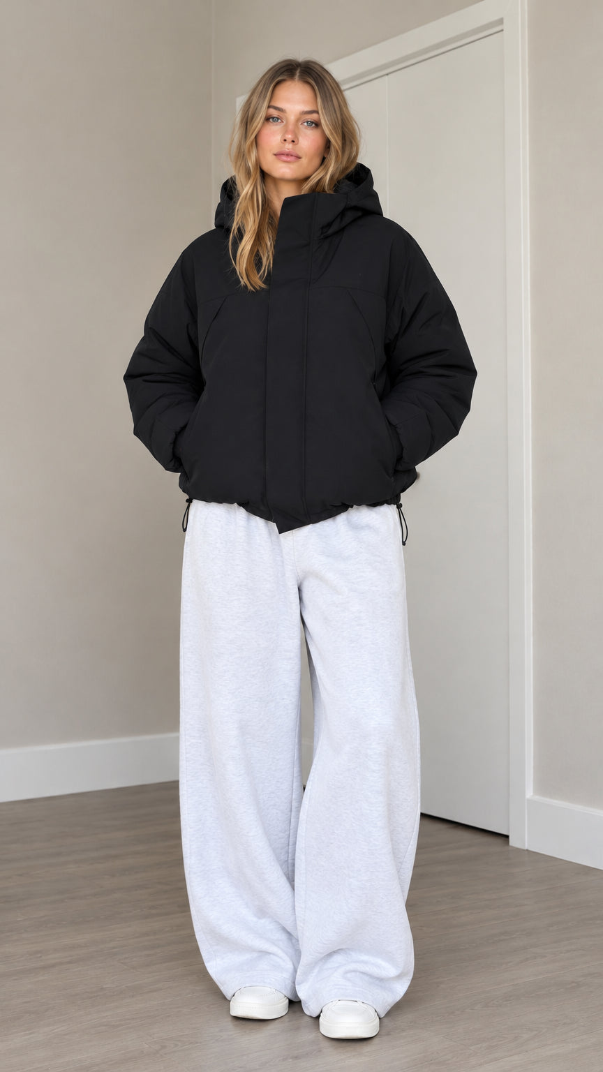 Front view of model wearing black hooded puffer jacket with drawstring hem and wide leg sweatpants