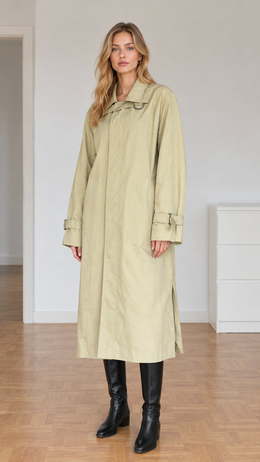 Front view of model wearing sage green relaxed longline trench coat with tall black boots