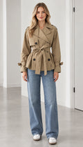 Front view of model wearing khaki short double-breasted trench coat with self-tie belt and wide-leg jeans