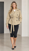Front full view of woman wearing khaki short double-breasted trench coat with tie belt