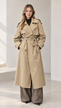Front full-length view of woman wearing a classic long khaki double-breasted trench coat with waist tie belt