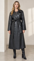 Front view of woman wearing long black faux leather belted trench coat with high boots