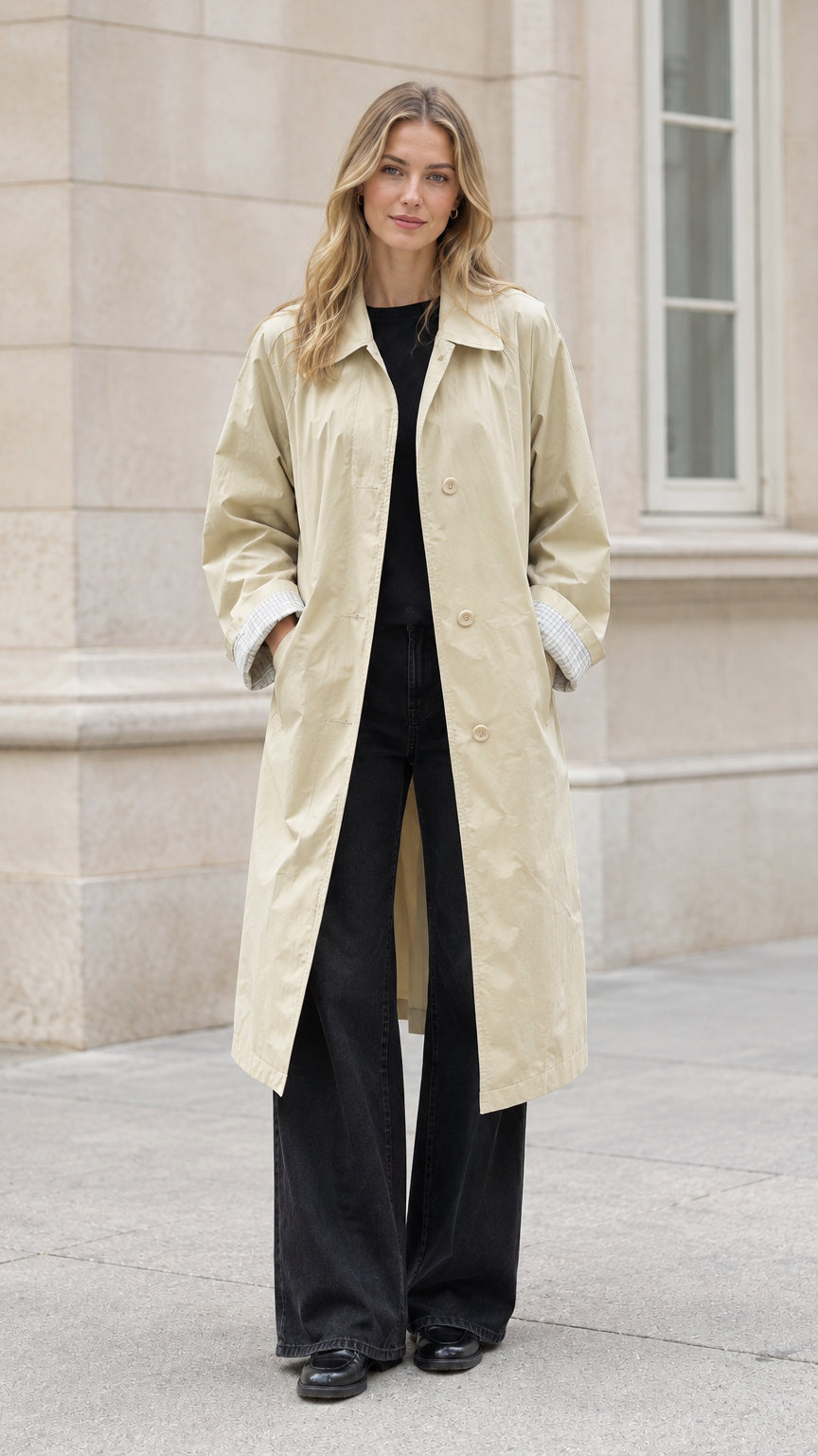 Front full-length view of model wearing a beige long belted trench coat with black wide-leg trousers