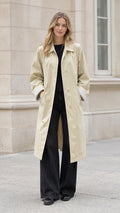 Front full-length view of model wearing a beige long belted trench coat with black wide-leg trousers