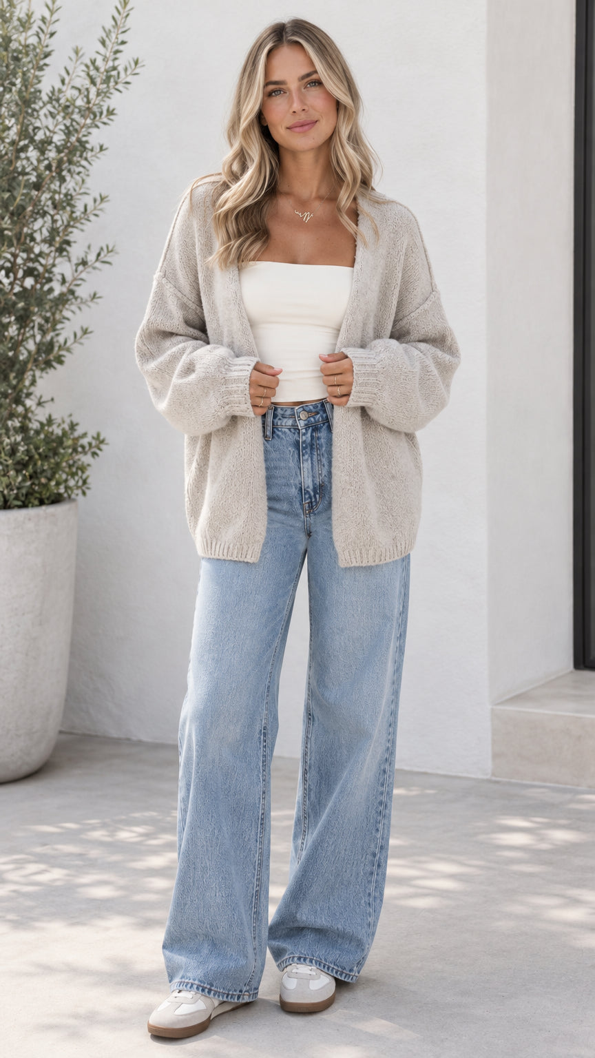 Front view of model wearing oatmeal open front oversized knit cardigan with light blue jeans