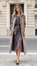 Full front view of model wearing taupe long trench coat over matching lace midi dress with belt