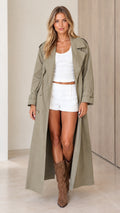 Full front view of a model wearing a sage green longline maxi trench coat open over a white crop top and shorts