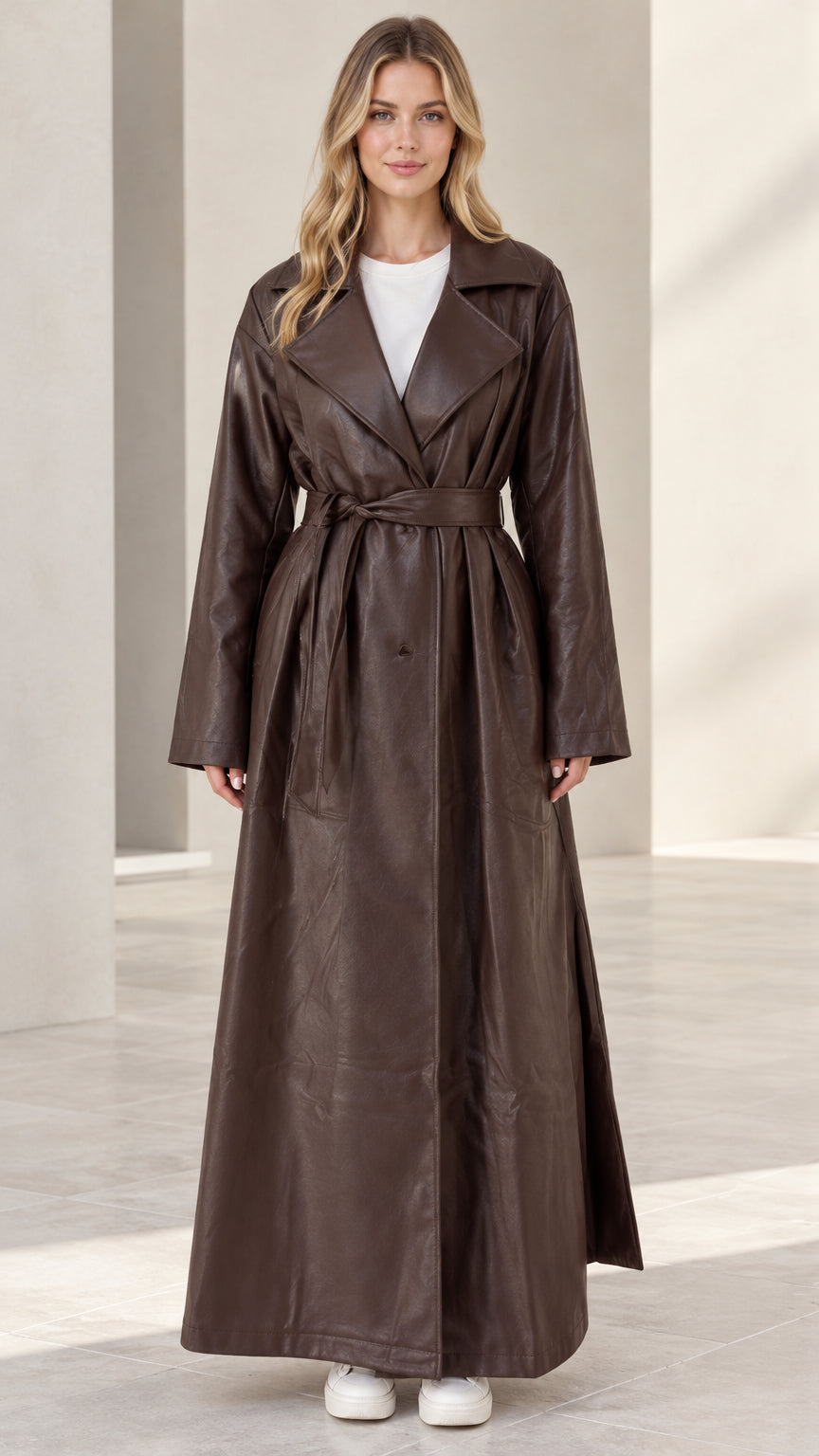 Front full-length view of woman wearing brown maxi faux leather belted trench coat