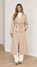 Full front view of a woman wearing a beige long double-breasted trench coat with tie belt