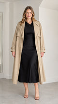 Front full-length view of woman wearing khaki longline trench coat over black dress