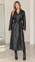 Front full-length view of model wearing black double-breasted faux leather maxi trench coat with tie belt