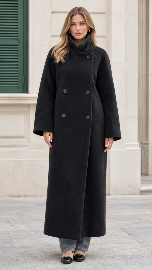 Full-front view of a woman wearing the black double-breasted funnel neck maxi overcoat