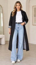 Front full-length view of woman wearing black longline trench coat with plaid cuffs over white top and jeans
