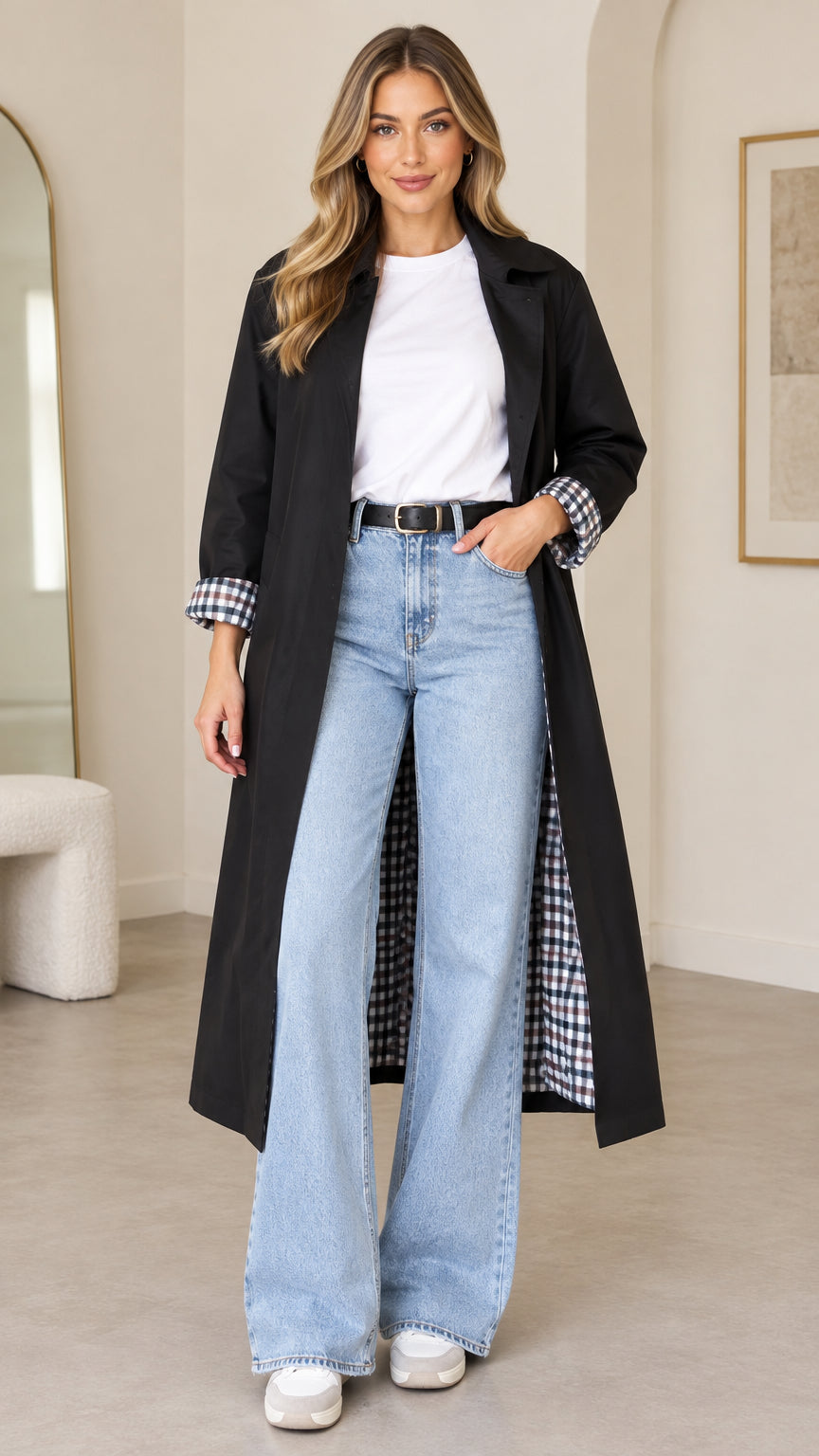 Front full-length view of woman wearing black longline trench coat with plaid cuffs over white top and jeans