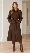 Front view of model wearing long brown double-breasted trench coat with tie belt
