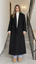 Full-length front view of woman wearing a black longline tailored maxi coat over a cream turtleneck and jeans