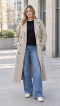 Front full-length view of model wearing khaki double-breasted trench coat with wide-leg jeans