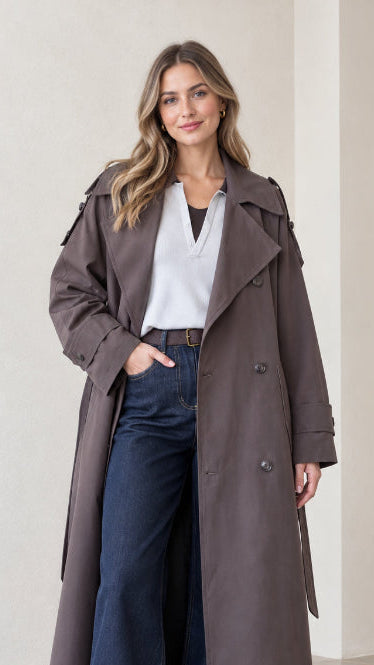 Front view of woman wearing full-length charcoal double-breasted trench coat with dark jeans