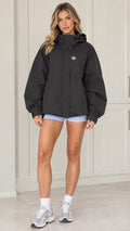 Front view of model wearing black oversized hooded windbreaker jacket