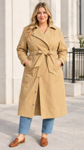 Front full-length view of woman wearing khaki plus size belted trench coat with denim jeans