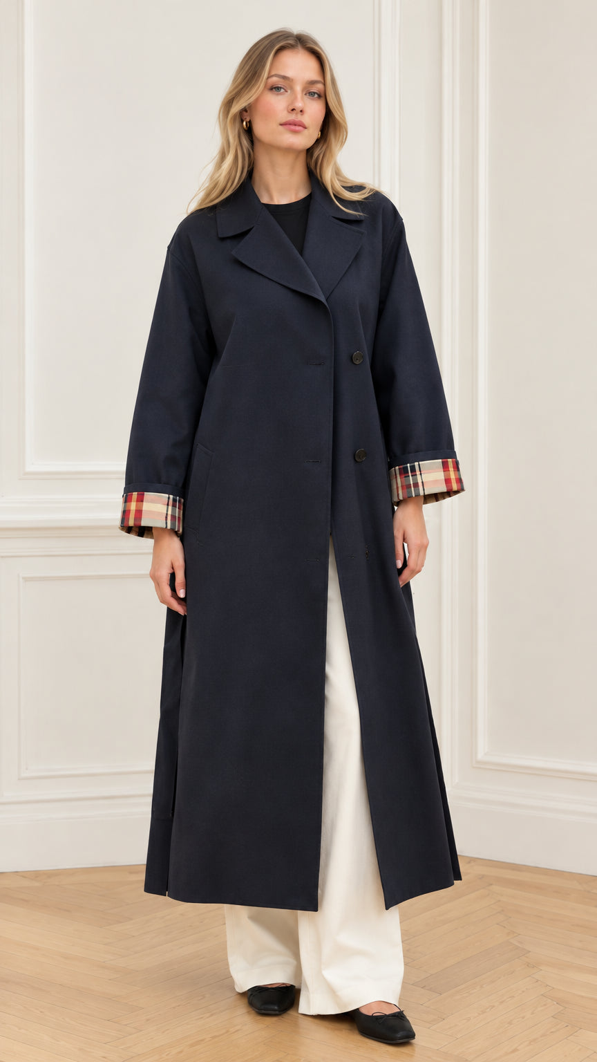 Front full-length view of woman wearing navy blue maxi trench coat with plaid cuffs