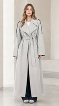 Front view of model wearing light grey maxi trench coat with tie belt