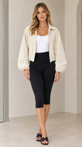 Front full-length view of model wearing beige cropped zip-up jacket with black capri leggings