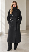 Front view of model wearing black double-breasted long overcoat with belted waist and high collar