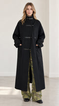 Front view of model wearing full-length black high-neck overcoat with buckle collar and camo trousers