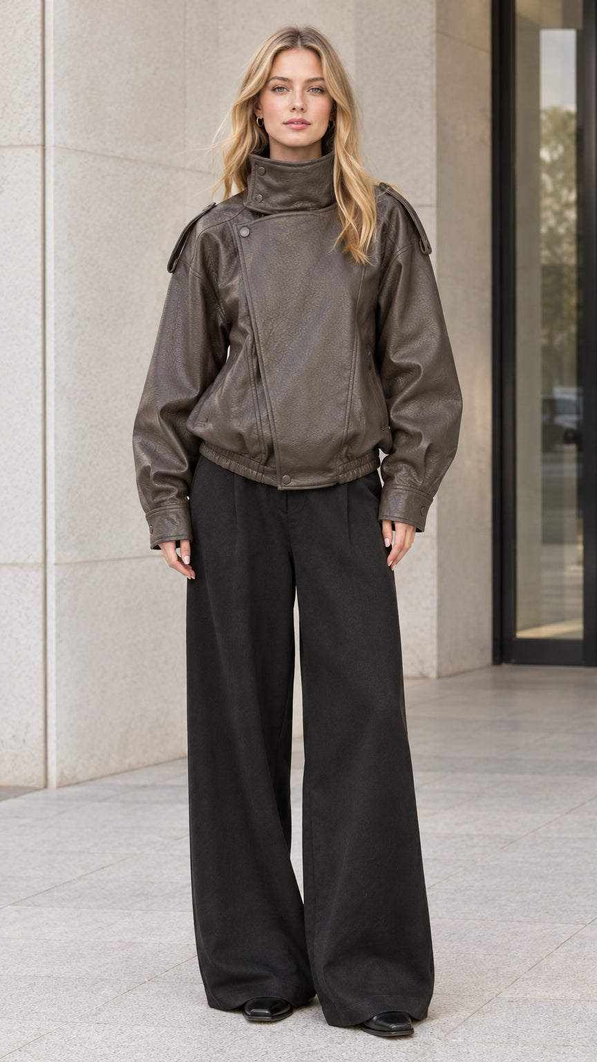Front full-body view of model wearing charcoal brown faux leather bomber jacket with high stand collar and black wide-leg trousers