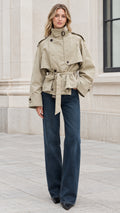 Front view of model wearing sage green cropped belted trench jacket with high collar and denim pants
