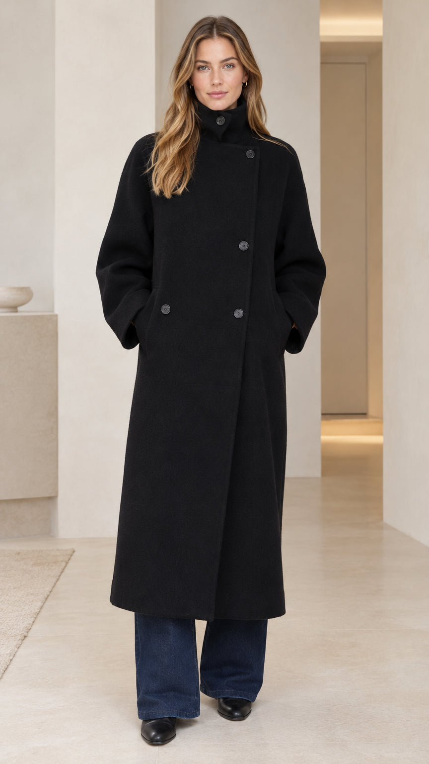 Front view of model wearing black high neck asymmetric longline overcoat with wide leg trousers