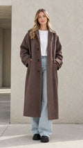 Full front view of model wearing a brown longline relaxed lapel overcoat with wide jeans