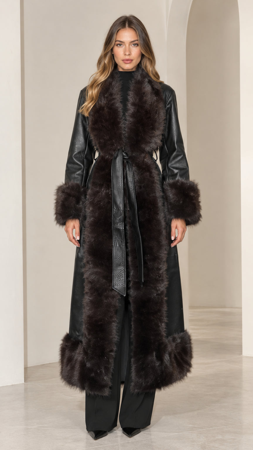 Model wearing long black faux leather coat with plush dark faux fur collar and trim
