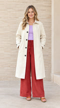 Front full-length view of woman wearing cream single-breasted long trench coat