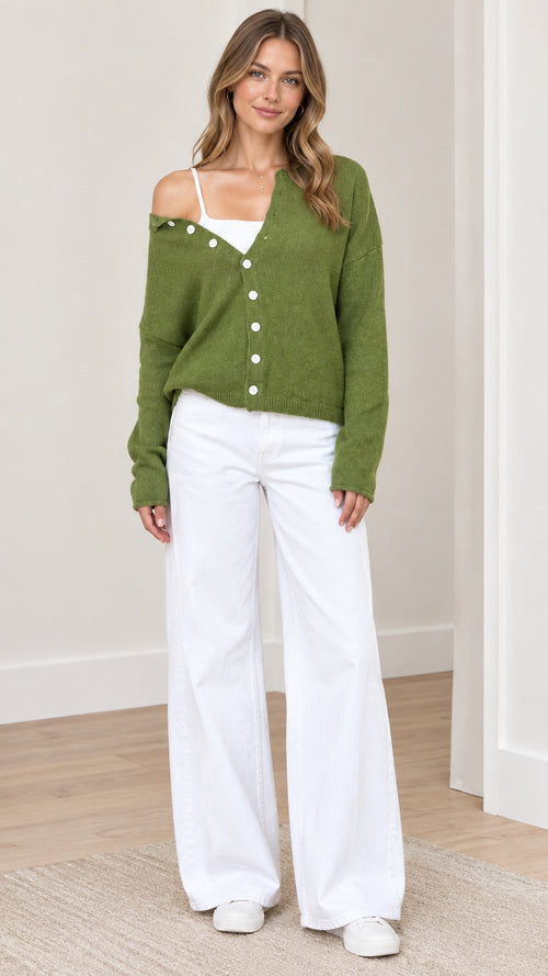 Front view of woman wearing green asymmetrical button-down knit cardigan sweater with white wide-leg pants