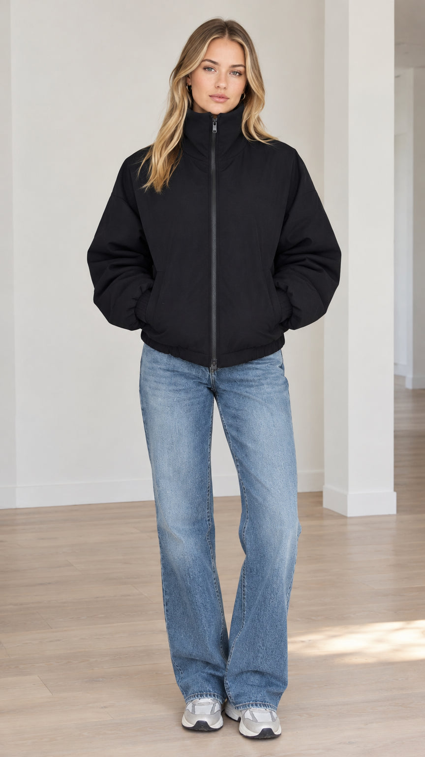 Front full-length view of model wearing black stand-collar zip-up padded jacket with wide-leg jeans