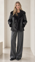 Front view of model wearing black faux shearling lapel jacket with wide-leg trousers