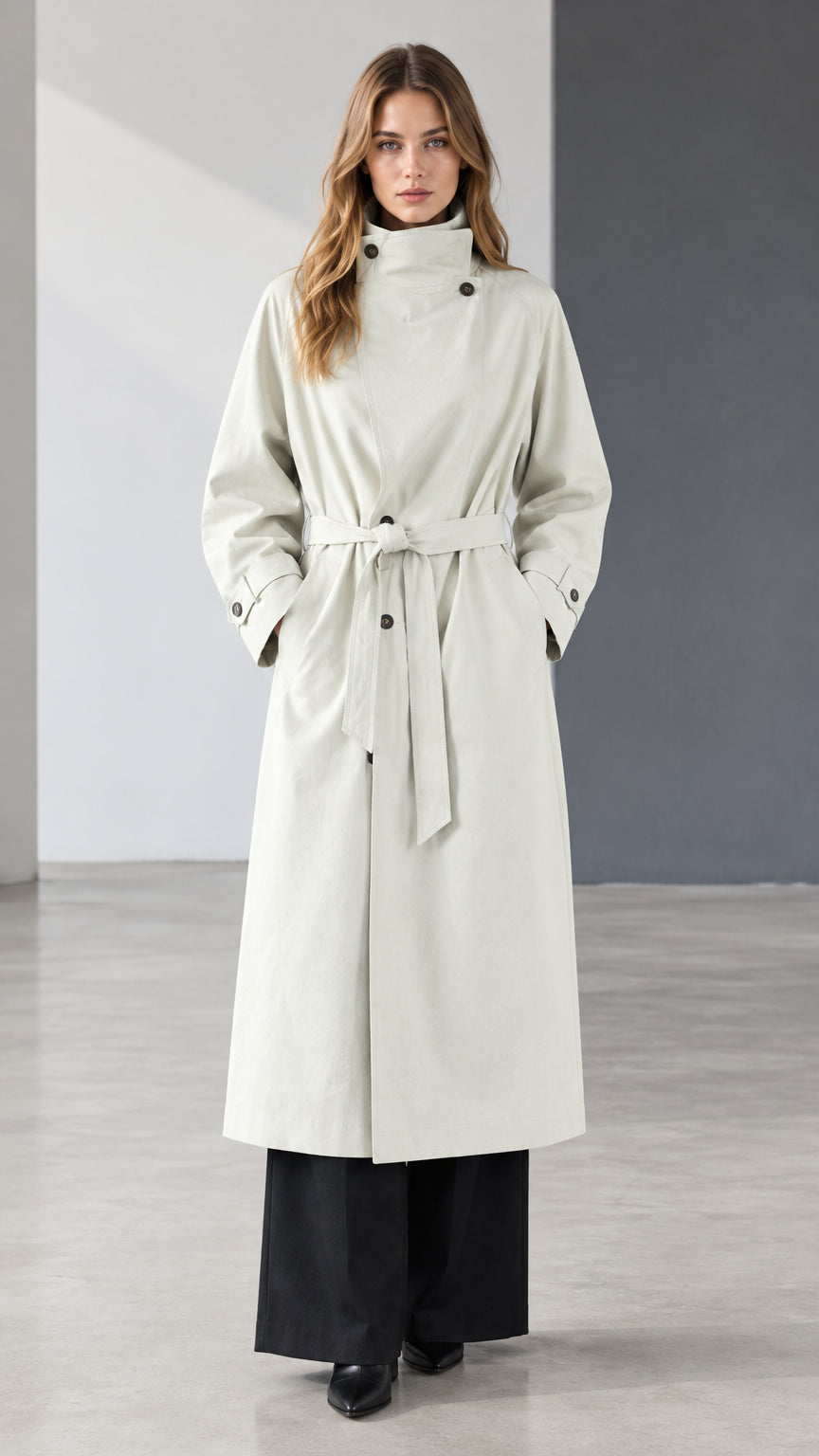 Front view of model wearing off white belted longline trench coat with high collar