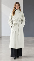 Front view of model wearing off white belted longline trench coat with high collar