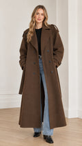 Front full-length view of woman wearing brown double-breasted maxi trench coat with denim and boots