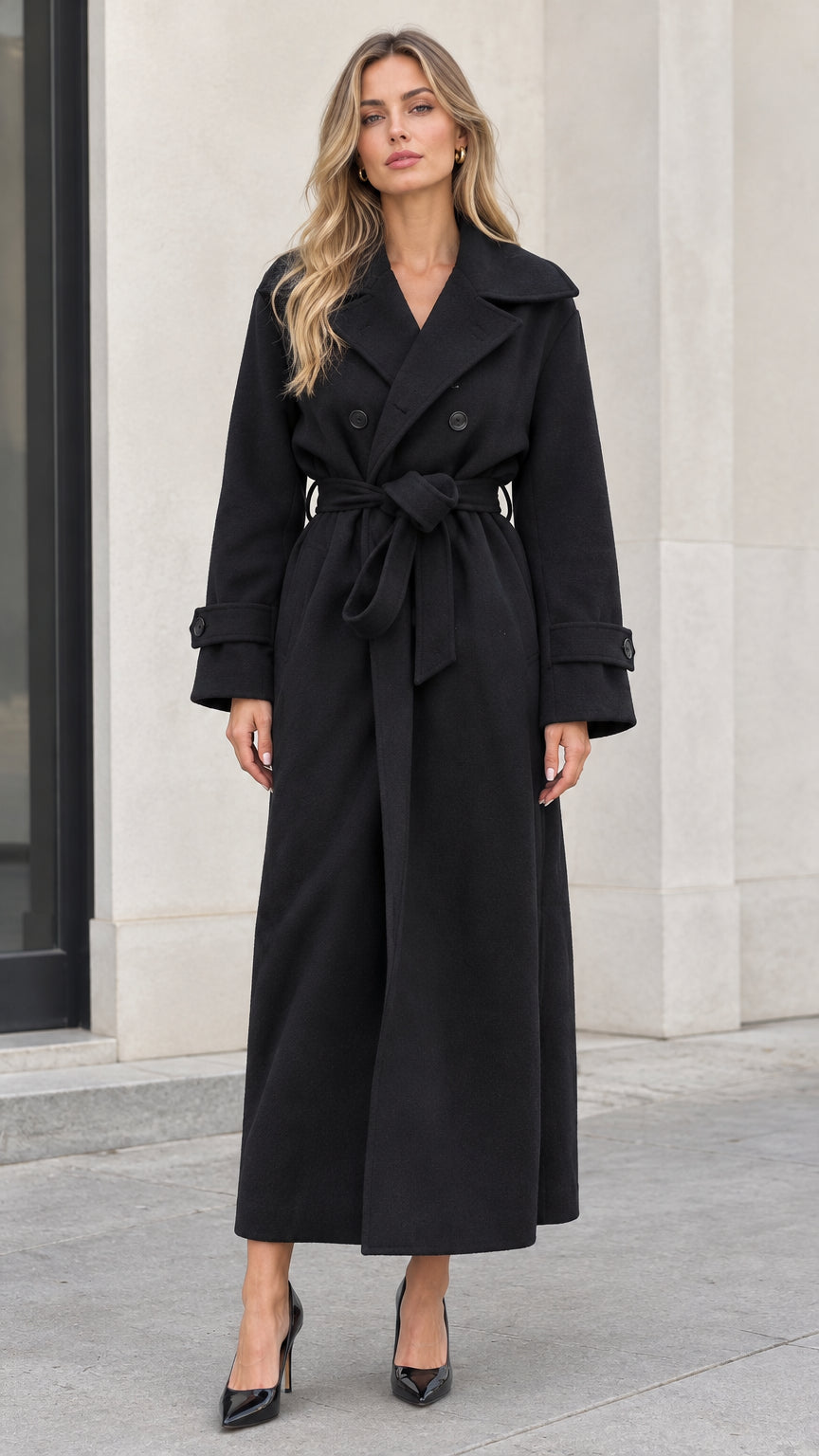 Front full-length view of woman wearing black double-breasted maxi overcoat tied at waist