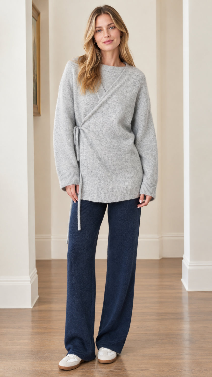 Front full view of woman wearing Light Gray asymmetrical side-tie knit tunic sweater with navy trousers