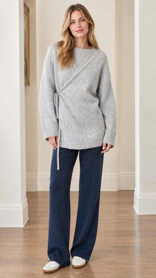 Front full view of woman wearing Light Gray asymmetrical side-tie knit tunic sweater with navy trousers