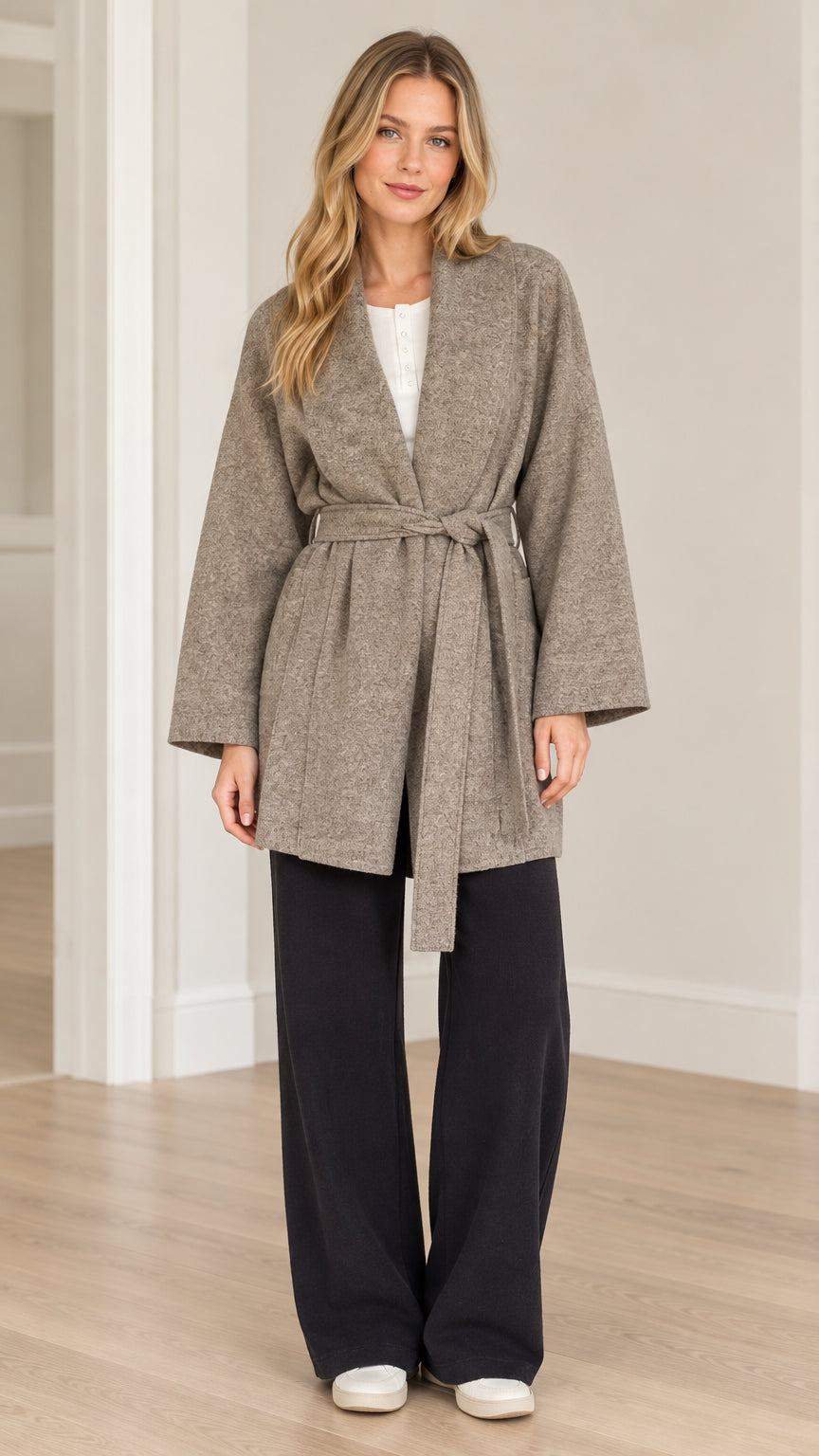 Full front view of model wearing taupe textured herringbone belted wrap coat with black wide-leg trousers