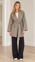 Full front view of model wearing taupe textured herringbone belted wrap coat with black wide-leg trousers