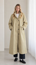 Front full view of woman wearing sage khaki longline trench overcoat with black pants and loafers