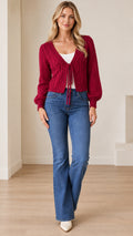 Full front view of a model wearing a burgundy cable knit cropped cardigan with tie-front detail and flare jeans