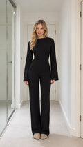 Front full-length view of model wearing black long-sleeve wide-leg jumpsuit with boat neckline