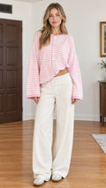 Front full-length view of model wearing pink striped knit button-front cardigan with white pants